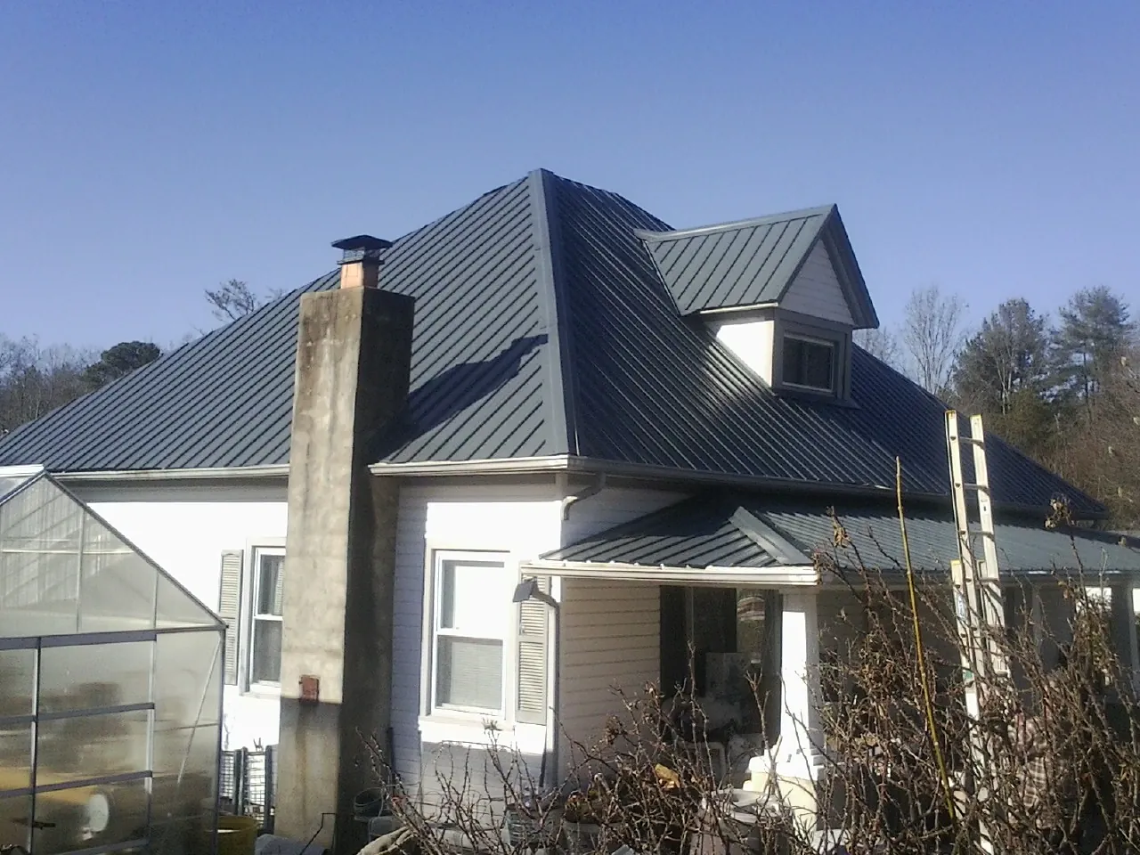 Dark blue standing seam metal roof on a white farmhouse with dormer — Slate & Tile Roof Repair by Roofing Brothers in Bleiblerville