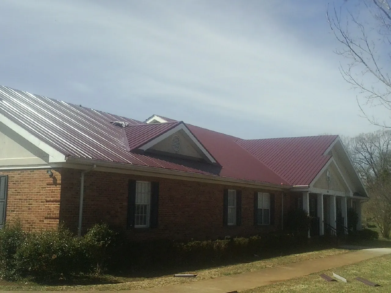 Red metal roof with gabled entries on a long brick building, from a Hail Damage Roof Repair job in Bleiblerville