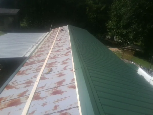 Old rusted panels beside newly installed green metal roofing — Wind Damage Roof Repair by Roofing Brothers in Bleiblerville