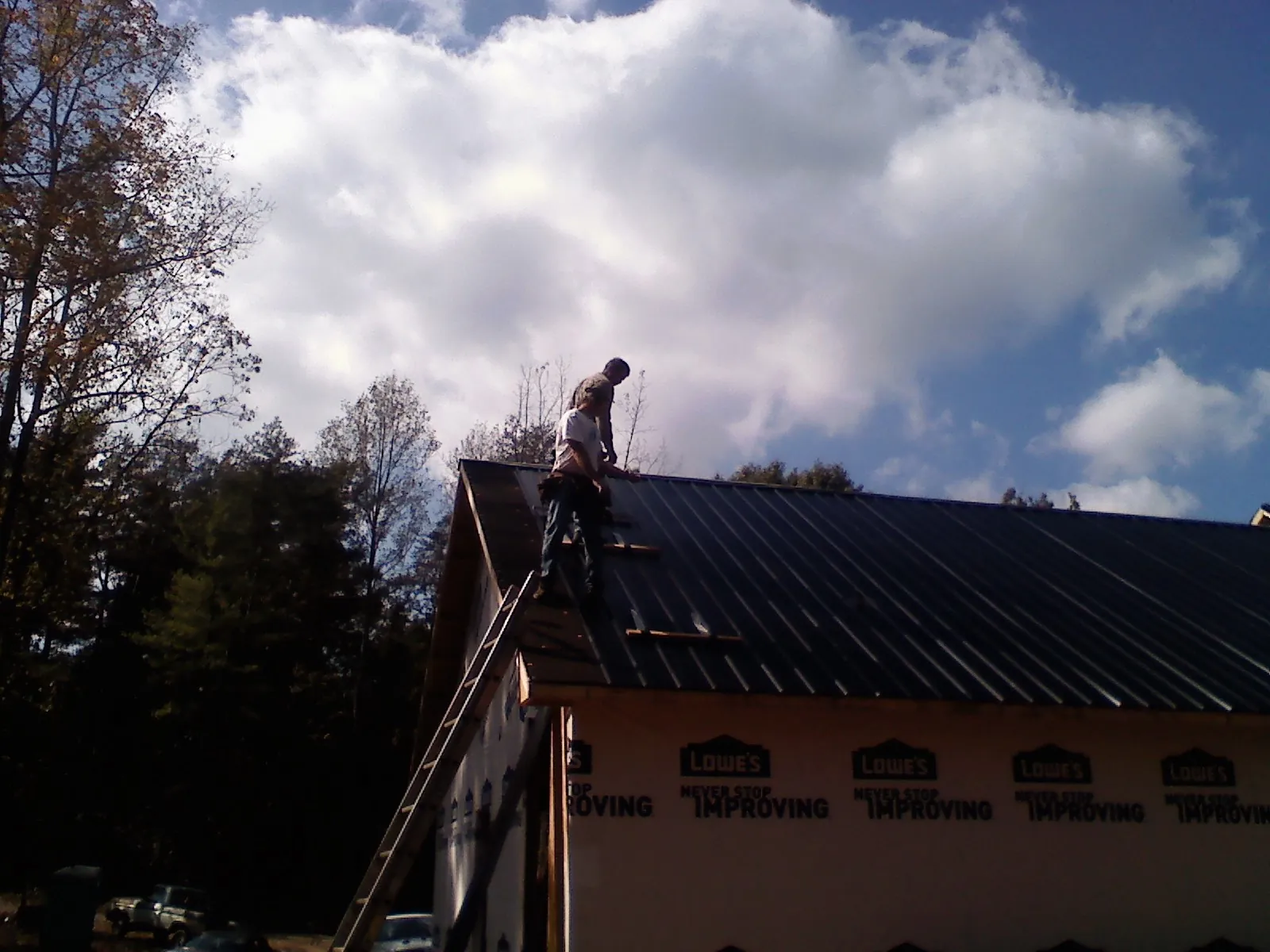 Roofer fastening dark metal panels high against a cloudy sky, from a Roof Inspection job in Bleiblerville
