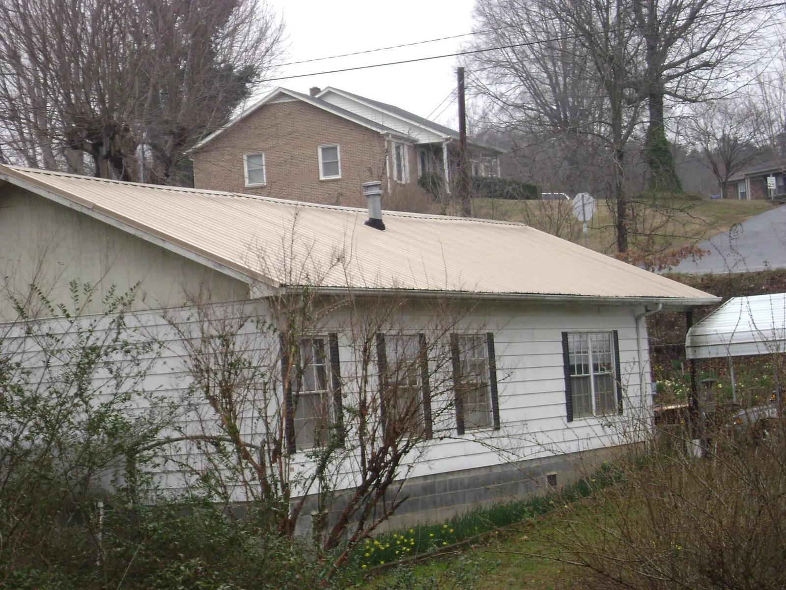 Tan metal roof on a white sided house set into a hillside — Commercial Roofing by Roofing Brothers in Bleiblerville