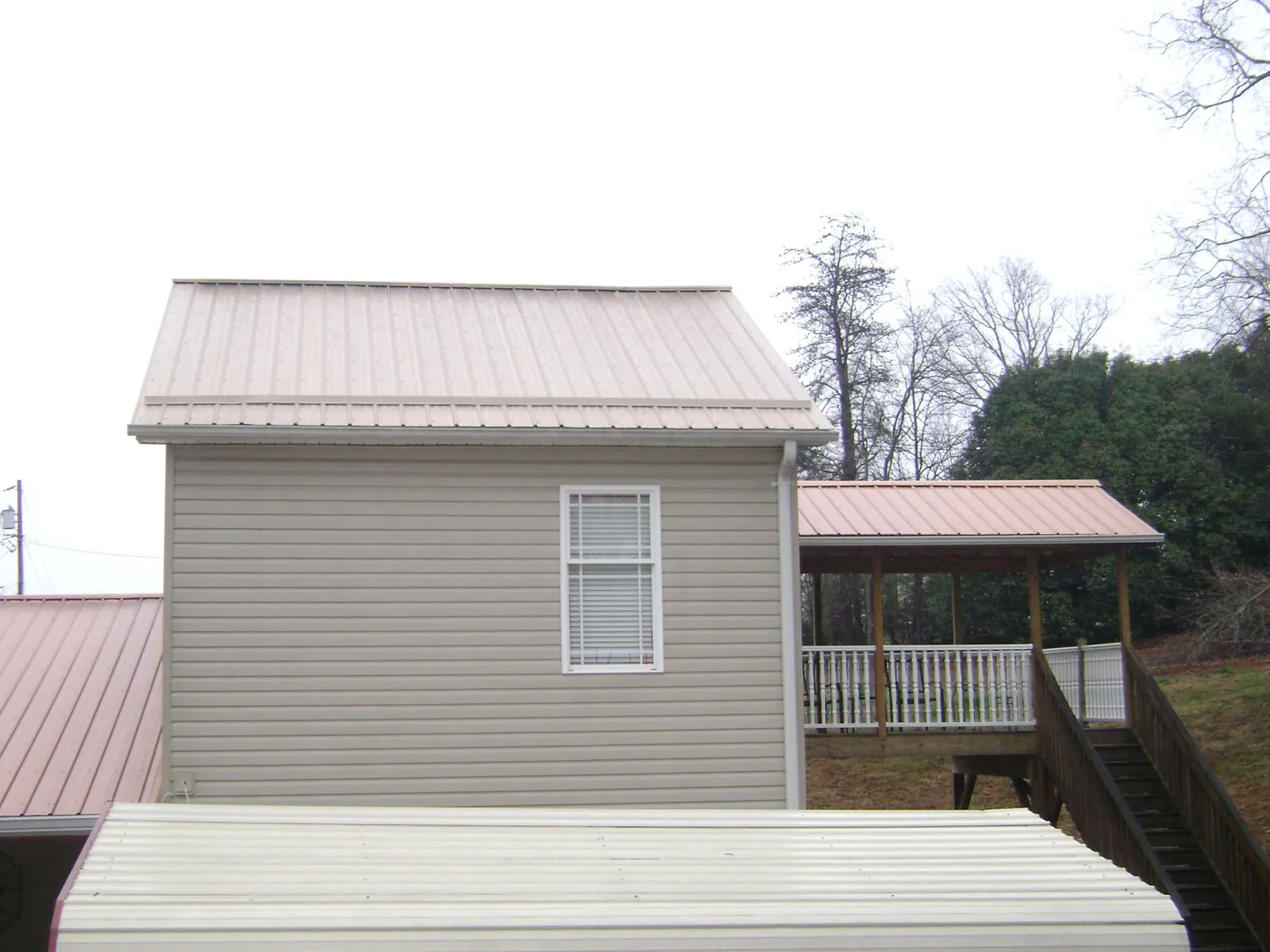 Tan metal roofs on a two story addition and attached porch, from a Roof Replacement job in Bleiblerville
